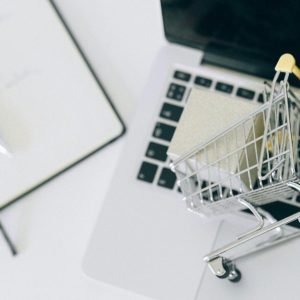Carrinho de compras em miniatura sobre laptop representando retail media networks e publicidade em marketplaces
