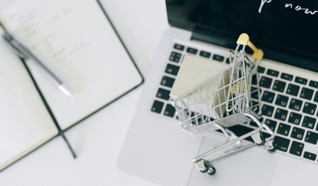 Carrinho de compras em miniatura sobre laptop representando retail media networks e publicidade em marketplaces