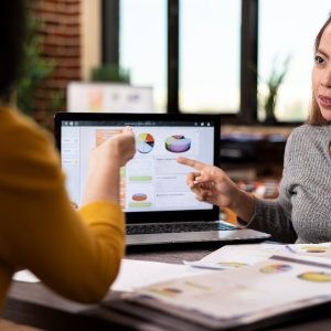 Gestor apontando para gráficos em laptop analisando leads qualificados no funil de vendas