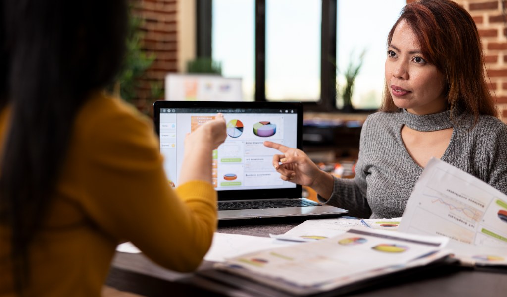 Gestor apontando para gráficos em laptop analisando leads qualificados no funil de vendas